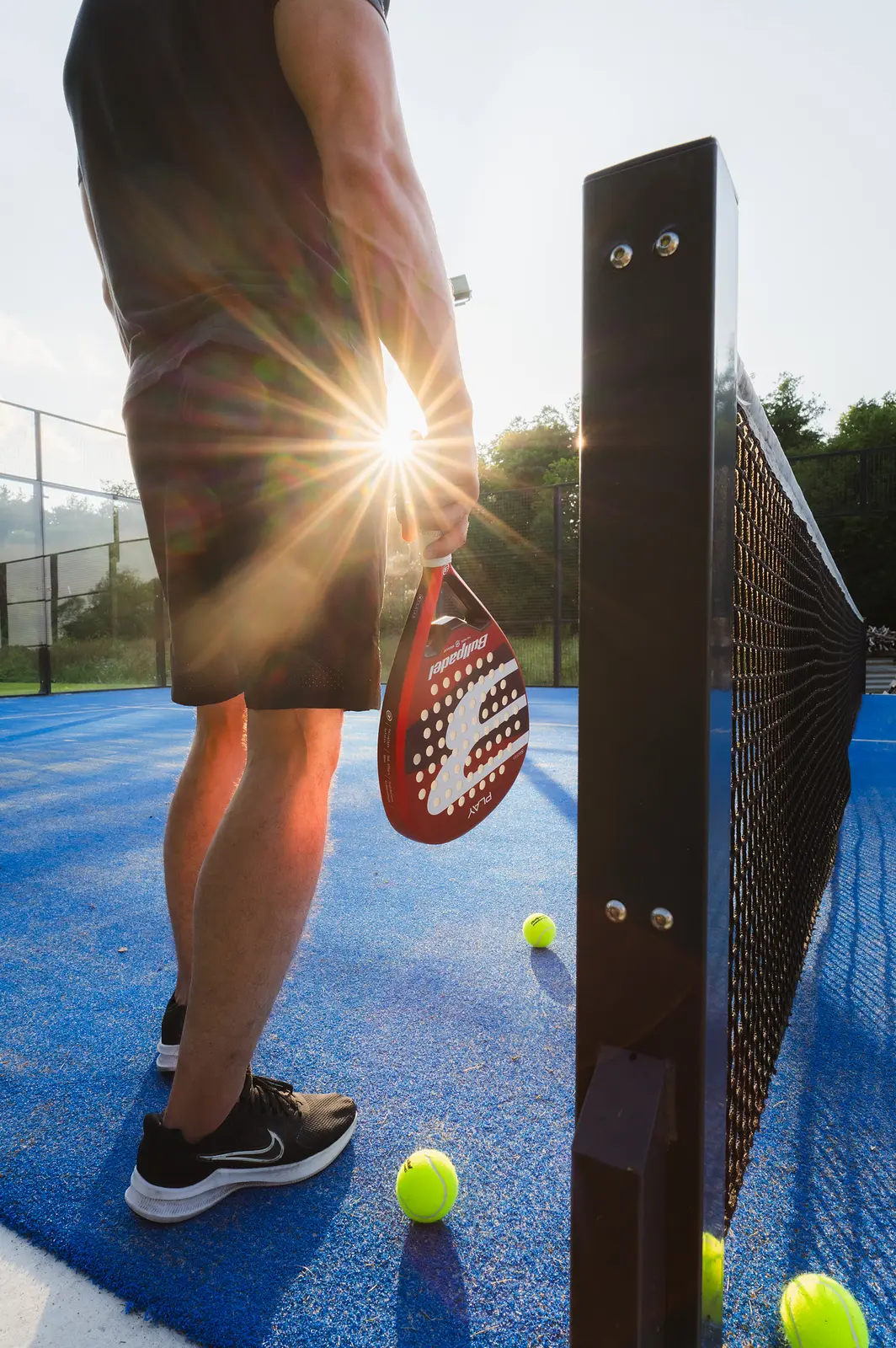Bullpadel raketė ir kamuoliukai ant korto vakaro saulėje